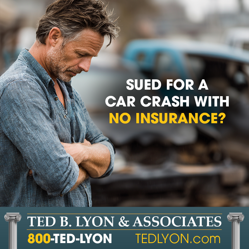A worried man stands with folded arms in front of a wrecked car.